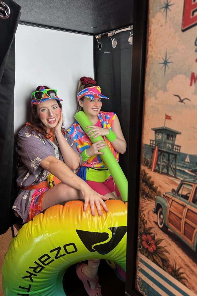 Two guests with beach props and an inflatable ring inside the enclosed photo booth